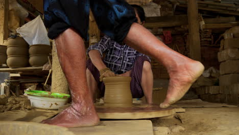 An-old-Asian-woman-handcrafts-a-new-vase-on-a-foot-powered-turning-table,-showcasing-the-cultural-art-of-pottery-and-tourism