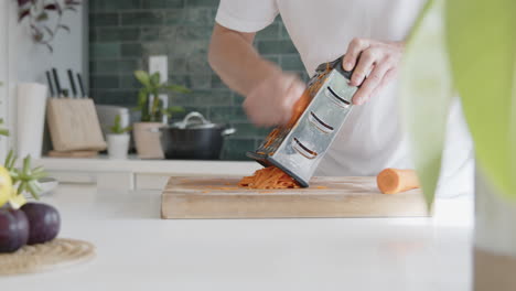 Mittlere-Aufnahme-Eines-Mannes,-Der-In-Einer-Modernen-Küche-Frische-Karotten-Mit-Einer-Reibe-Reibt
