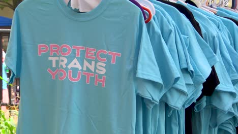 A-medium-close-up-shot-of-a-rack-of-blue-tee-shirts-with-the-logo-Protect-Trans-Youth-featuring-diversity,-equity-and-inclusion
