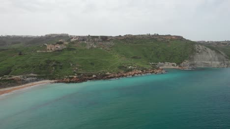 Tropical-Beach-At-The-Base-Of-A-Mountain-With-Turquoise-Water-In-Malta,-Gozo-Island