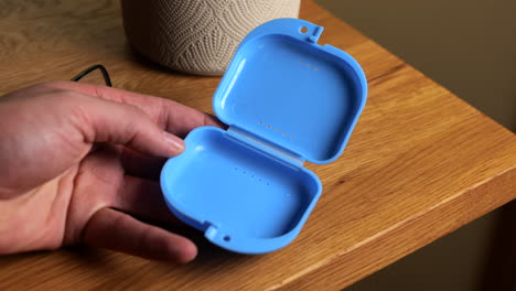 Hand-putting-transparent-dental-teeth-protector-into-carry-case-on-wooden-table