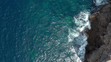 Blick-Von-Oben-Nach-Unten-über-Eine-Felsige-Küste-In-Malta,-Mit-Plätschernden-Wellen-Und-Türkisfarbenem,-Kristallklarem-Wasser