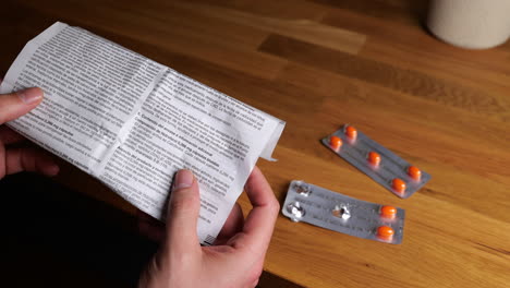 Hands-holding-medicine-guide-sheet-with-blister-pack-of-orange-medication-tablets-on-wooden-table