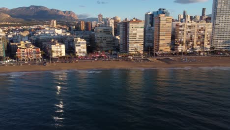 Lateral-side-aerial-view-of-beachfront-line-of-buildings-in-Benidorm-bay-at-golden-hour