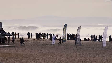Wide-shot,-Billabong-surf-championship,-crowded-on-the-beach-with-a-big-and-strong-waves-behind,-Carcavelos-beach,-Cascais,-Portugal