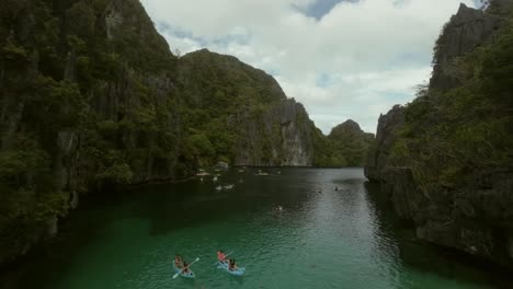 Drone-flyover-group-of-tourists-exploring-El-Nido-scenery-by-kayak,-Philippines