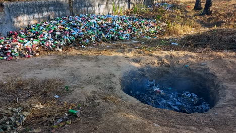 Hole-in-the-earth-burning-garbage,-bottles-and-beverage-cans