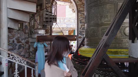 Woman-in-blue-dress-Hits-Buddhist-Bell-With-Suspended-Log-Inside-The-Linh-Phuoc-Temple-In-Vietnam