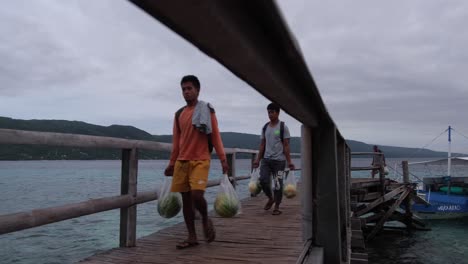 Philippinische-Einheimische-Gehen-Auf-Einem-Hölzernen-Pier-Und-Tragen-Waren,-Die-Von-Einem-Angedockten-Boot-Auf-Der-Insel-Sumilon,-Cebu,-Philippinen,-Ausgestiegen-Sind