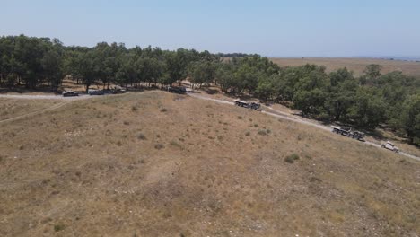 Israel-Army-infantry-squad-soldiers-on-vehicle-driving-through-green-field-at-training-ground-country-road,-Aerial-Tracking-shot