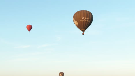 Nach-Unten-Geneigte-Luftaufnahme-Von-Heißluftballons,-Die-Bei-Sonnenaufgang-Am-Morgen-über-Die-Malerische-Landschaft-Von-Myanmar-Fliegen