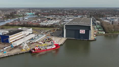 Large-Red-Transport-Boat-Offloading-Cargo-at-Warehouse,-Rotterdan,-Holland,-Aerial-Wide-Angle-Shot