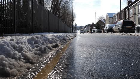 A-stream-of-water-by-the-side-of-a-road-as-snow-and-slush-melts-in-the-sun