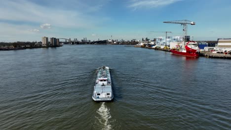 Barco-De-Carga-Que-Transporta-Mercancías-Por-El-Canal,-Rotterdam,-Tiro-Medio-Aéreo-Siguiendo-El-Barco