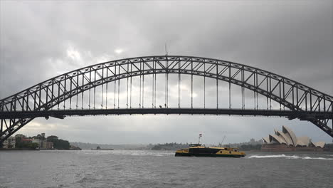 A-ferry-passes-by-Sydney-harbour-bridge-and-opera-house-on-a-rainy-overcast-day,-Australia