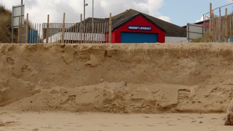 Coastal-erosion-of-Sandunes-on-Hemsby-Beach,-with-Hemsby-lifeboat-station-in-background,-Wide-shot