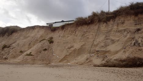 Erosión-Costera-De-Sandunes-En-La-Playa-De-Hemsby-Con-Casa-Al-Borde-De-Un-Acantilado,-Plano-General