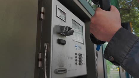 Man-picks-up-a-pay-phone-at-the-bus-stop-in-day-time