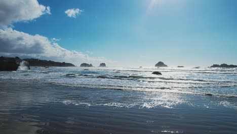 Crashing-waves-spread-and-glide-across-Bandon-Oregon-beach,-strong-midday-sun