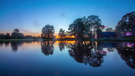 Time-lapse-shot-of-beautiful-golden-sunset-behind-tranquil-lake-in-wilderness-in-the-evening---Tree-Silhouette-reflection-on-water-surface