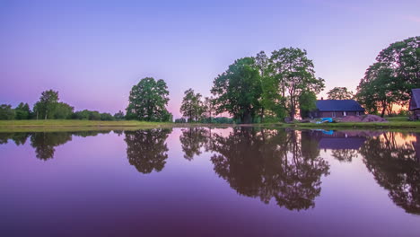 Relaxing-day-to-dawn-time-lapse-on-a-reflective-lake-with-small-house-and-trees