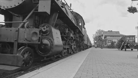 A-Black-and-White-View-of-Antique-Steam-Passenger-Train,-With-a-Low-Camera-Angle,-Arriving-into-a-Train-Station,-Blowing-Smoke-on-a-Winter-Day