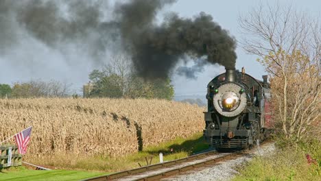 A-View-of-an-Approaching-Antique-Steam-Passenger-Train,-Blowing-Black-Smoke,-Passing-Corn-Fields,-Waiting-to-be-Harvested,-on-a-Sunny-Fall-Day
