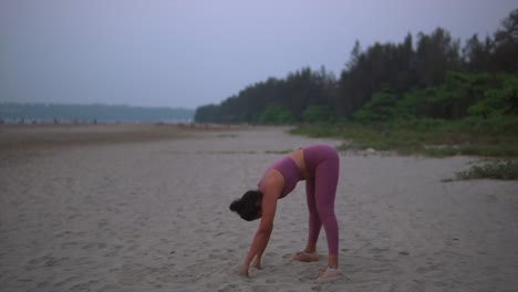 Young-Indian-Lady-Doing-Yoga-Routine-Stretches-on-Beach-Sand-at-Dusk,-Dawn