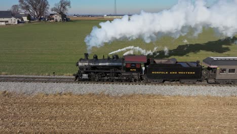 An-Aerial-Side-View-of-a-Steam-Passenger-Train-Traveling,-in-Slow-Motion,-Blowing-Smoke,-while-Traveling-Thru-the-Countryside,-on-a-Sunny-Winter-Day