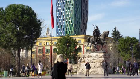 Pedestrians-walking-on-main-square-of-Tirana-capital-city-near-Skanderbeg-statue,-Spring-sunny-day