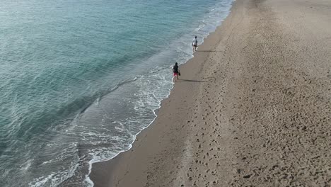 Aerial-views-over-a-beach-with-gentle-waves-and-people-walking-along-the-shore-calmly