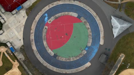 A-top-down-view-directly-above-a-circular-track-and-sports-field-in-an-empty-park-on-a-cloudy-day