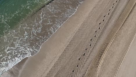 Luftaufnahmen-über-Einen-Strand-Mit-Sanften-Wellen-Und-Menschen,-Die-Ruhig-Am-Ufer-Entlang-Gehen