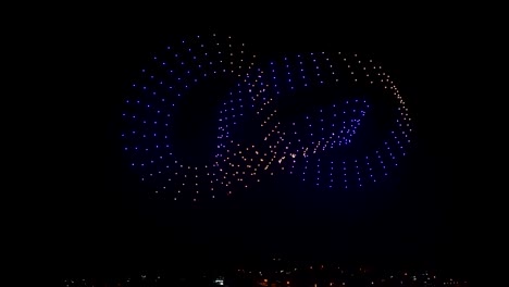 Fliegende-Drohnen-Erstellen-3D-Modelle,-Die-Sich-Am-Nachthimmel-über-Den-Lichtern-Der-Stadt-Bewegen,-Eine-Außergewöhnliche-Show