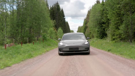 DRONE-FRONT--A-Tesla-Model-3-drives-down-a-forested-dirt-road