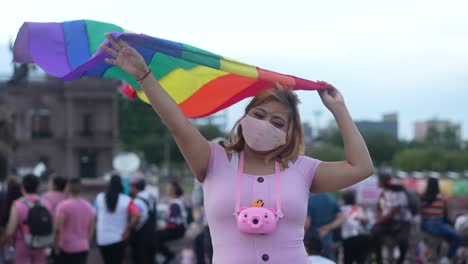 Lesbische-Latino-Frau-Mit-Rosa-Maske,-Die-Die-Homosexuellen-Stolz-Gay-Parade-Mit-Großer-Regenbogenfahne-Unterstützt