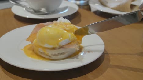 hand-of-woman-cutting-fresh-egg-benedict-poached-egg-for-breakfast