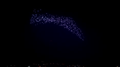 Drohnen-Mit-Hellen-Lichtern-Erzeugen-Abstrakte-Modelle-Am-Nachthimmel,-Die-über-Die-Stadt-Fliegen