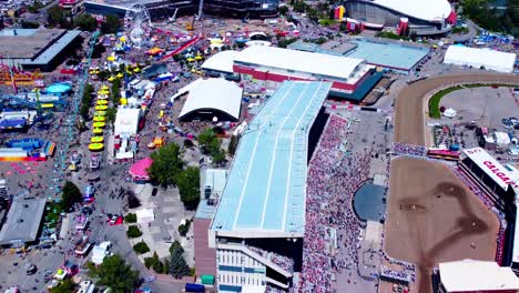 aerial-flyover-Calgary-Stampede-fair-overlooking-horseback-races-from-the-grand-stands-to-the-mass-crowds-of-people-lined-up-for-food-and-fun-rides-on-a-bright-sunny-afternoon