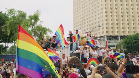 Weißer-Lastwagen-Mit-Bühne,-Der-Die-Teilnehmer-Der-Pride-Parade-An-Einer-Großen-Menschenmenge-Entlang-Der-Avenue-Juárez-Vorbeiführt,-Die-Regenbogenfahnen-In-Mexiko-Stadt-Schwenkt