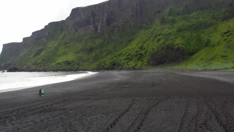 Vik,-Iceland-black-sand-beach-with-two-people-with-drone-video-moving-forward