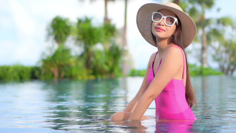 Beautiful-Classy-Exotic-Woman-in-Pink-Swimsuit-in-Swimming-Pool-of-Tropical-Resort