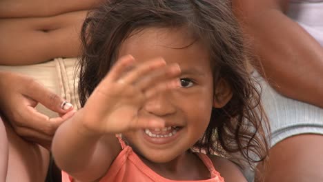 Nahaufnahme-Eines-Jungen-Indigenen-Amazonischen-Mädchens,-Das-Lächelnd-Mit-Seinen-Eltern-Sitzt-Und-Hallo-Winkt