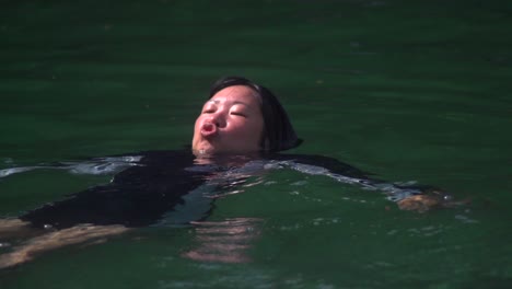 Asian-woman-wearing-swimsuit-and-floating-in-river-water-while-making-cute-faces-filmed-in-slow-motion
