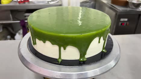Japanese-matcha-green-tea-mirror-glaze-drippy-chiffon-sponge-cake-spinning-on-revolving-turntable,-commercial-bakery-shot