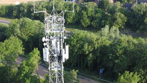 5G-cellular-tower-antenna-in-British-countryside-with-vehicles-travelling-on-highway-background-aerial-dolly-left-view