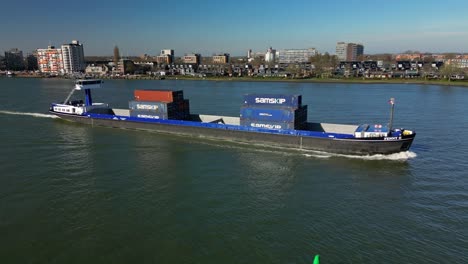 Aerial-shot-of-a-transportation-ship-with-containers-navigating-towards-the-city-Dordrecht,-The-Netherlands