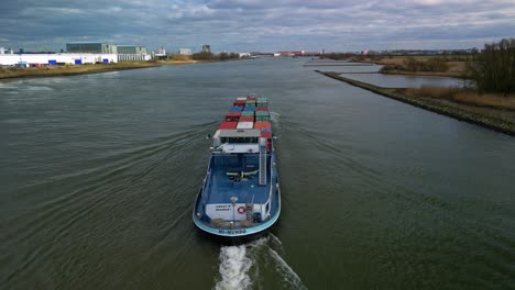 Aerial-view-following-the-big-cargo-ship-with-containers-through-the-canals-of-Zwijndrecht,-The-Netherlands