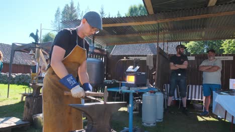 Blacksmith-manually-forging-the-molten-metal-on-the-anvil-in-smithy-with-spark-fireworks-outdoor-on-Elverum-city-in-Norway