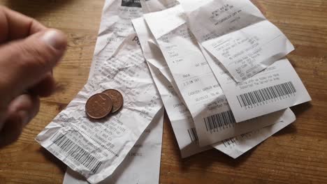 Hands-placing-coins-on-pile-of-spending-receipts-UK-cost-of-living-crisis